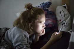 Teenage girl looks on her smartphone in bed during the night