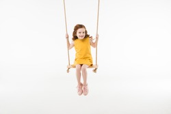 Little stylish child in dress riding on swing isolated on white