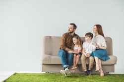 family with two kids sitting on couch and looking away on grey