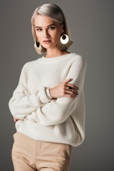 attractive girl posing in white knitted sweater and round earrings, isolated on grey