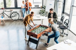 high angle view of young casual business people playing table football at office and having fun together