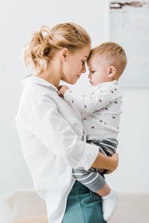 attractive mother embracing adorable toddler son at home
