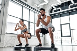 low angle view of concentrated sportive young couple in sportswear training with step platforms in gym 