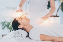 side view of calm young woman receiving reiki healing therapy on head and chest 