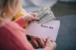 cropped view of senior couple holding envelope with 'roth ira' lettering and dollar banknotes