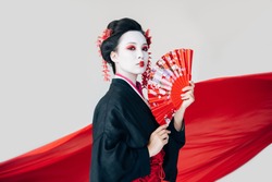 beautiful geisha in black kimono with hand fan and red cloth on background isolated on white