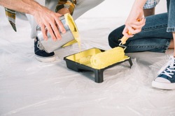 cropped view of man adding yellow paint into roller tray and woman holding paint roller