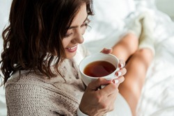 attractive woman in grey sweater holding cup of tea at morning 