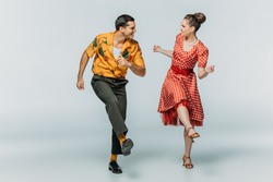 stylish dancers looking at each other while dancing boogie-woogie on grey background