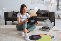 smiling girl holding vinyl record while chilling at home