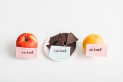Fresh apple, orange and chocolate with calories on cards on white background, calorie counting diet