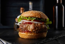  selective focus of tasty burger on dark surface, beer, vinegar and oil bottles isolated on black