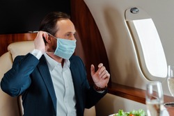 Selective focus of businessman putting on medical mask near champagne and salad on table in airplane