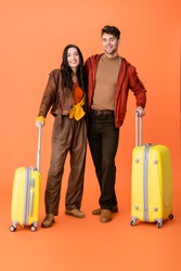 full length of stylish couple in autumn outfit standing near yellow baggage on orange