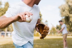 cropped view of man in leather glove playing baseball with teenager son in park