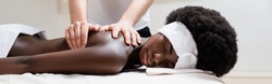 Masseur massaging african american woman wearing white headband in spa salon, banner