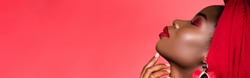 profile of african american young woman in stylish outfit and turban with closed eyes isolated on red, banner
