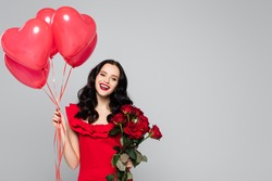 happy woman holding red heart-shaped balloons and roses isolated on grey
