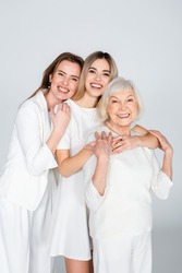 three generation of smiling women looking at camera and hugging isolated on grey