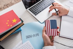 partial view of interpreter holding digital translator with usa flag emblem near paper with chinese hieroglyphs.Translation: 'international contract'