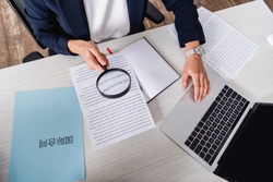 partial view of interpreter holding magnifier near paper with english text and laptop.Translation: 'international contract'