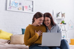 happy teenage girl and mother watching comedy movie on laptop in bedroom