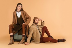 trendy woman sitting on vintage tv set near stylish man on floor on beige background