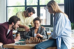 Smiling african american businesswoman playing chess near colleague pointing with finger and business people in office