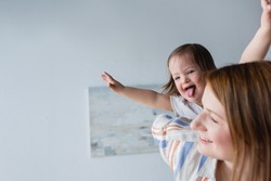 Kid with down syndrome sticking out tongue near blurred mother at home