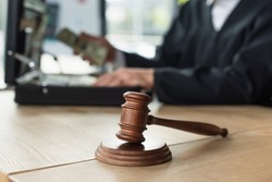 selective focus of wooden gavel near cropped judge and briefcase with money on blurred background, anti-corruption concept