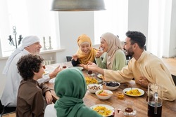 young arabian man talking to cheerful multicultural muslim family during dinner