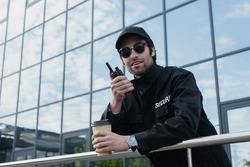 smiling guard with takeaway drink talking on walkie-talkie outdoors