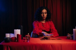 medium holding hand over tarot cards near candles and essential oils on dark background