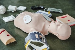 CPR training manikin near automated external defibrillator, wound care simulators, neck brace and bandages of floor in training room, medical equipment for first aid training and skills development
