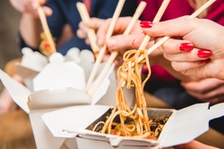 Close-up view of people eating noodles with chopsticks 