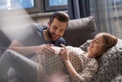 Happy man touching belly of smiling pregnant woman lying on sofa  