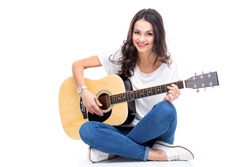 Smiling young woman sitting and playing guitar isolated on white