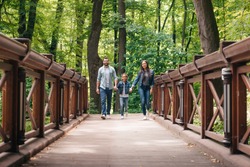 young interracial family holding hands and walking through the wooden bridge in forest