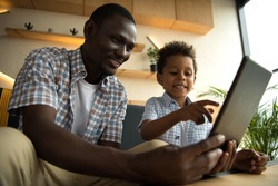 smiling african american father and son using digital tablet in cafe