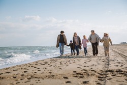 big multigenerational family walking together on beach at seaside