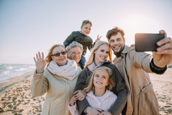 multigenerational family taking selfie on smartphone at seaside