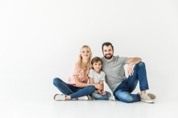 happy young parents with adorable little son sitting together isolated on white