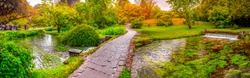 enchanted eden garden path bridge trail over pond in horizontal panoramic garden .