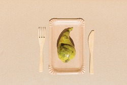 Pear wrapped in polyethylene plastic on the beige paper background. Immature, tasteless or inedible food concept. Copy space. Flat lay.