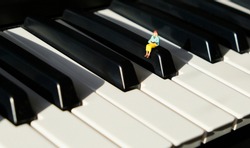 Miniature figurine of a woman sitting and reading on the keys of a piano.