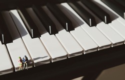 Miniature figurines of an elderly couple, sitting together on the keys of a piano.