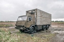 Old damaged Soviet refrigerator truck in field. Abandoned car under rain, cargo truck