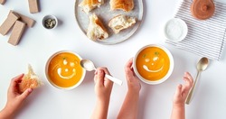 Children eat pumpkin cream soup with cartoon smiles from cream, no face