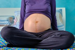 The belly of a Caucasian pregnant girl on the bed. It is visible the Linea 