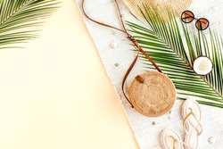 Woman's beach accessories:  rattan bag, straw hat, tropical palm leaves on yellow background. Summer background. Flat lay, top view.